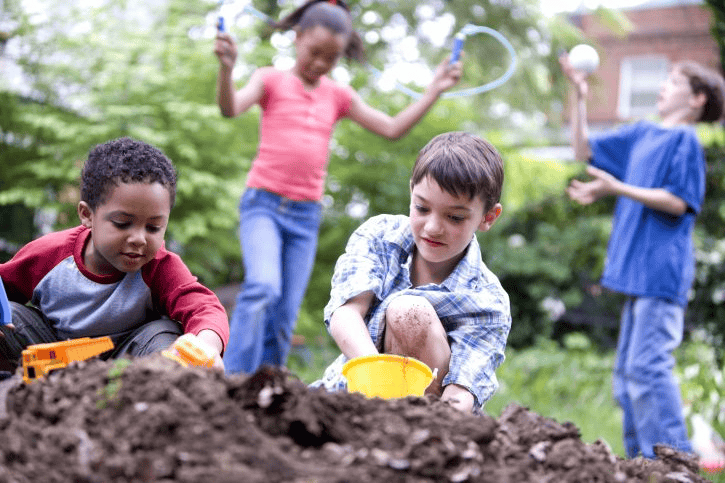 Four children engaged in outdoor play, digging in dirt and interacting socially.