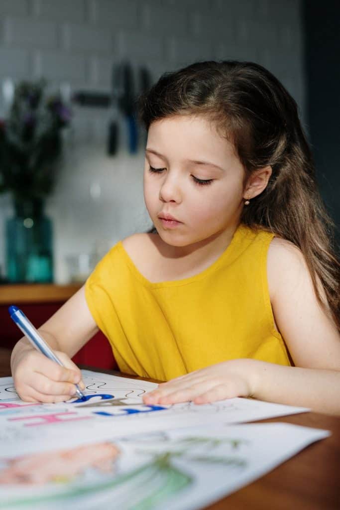 girl in yellow tank top writing on white paper