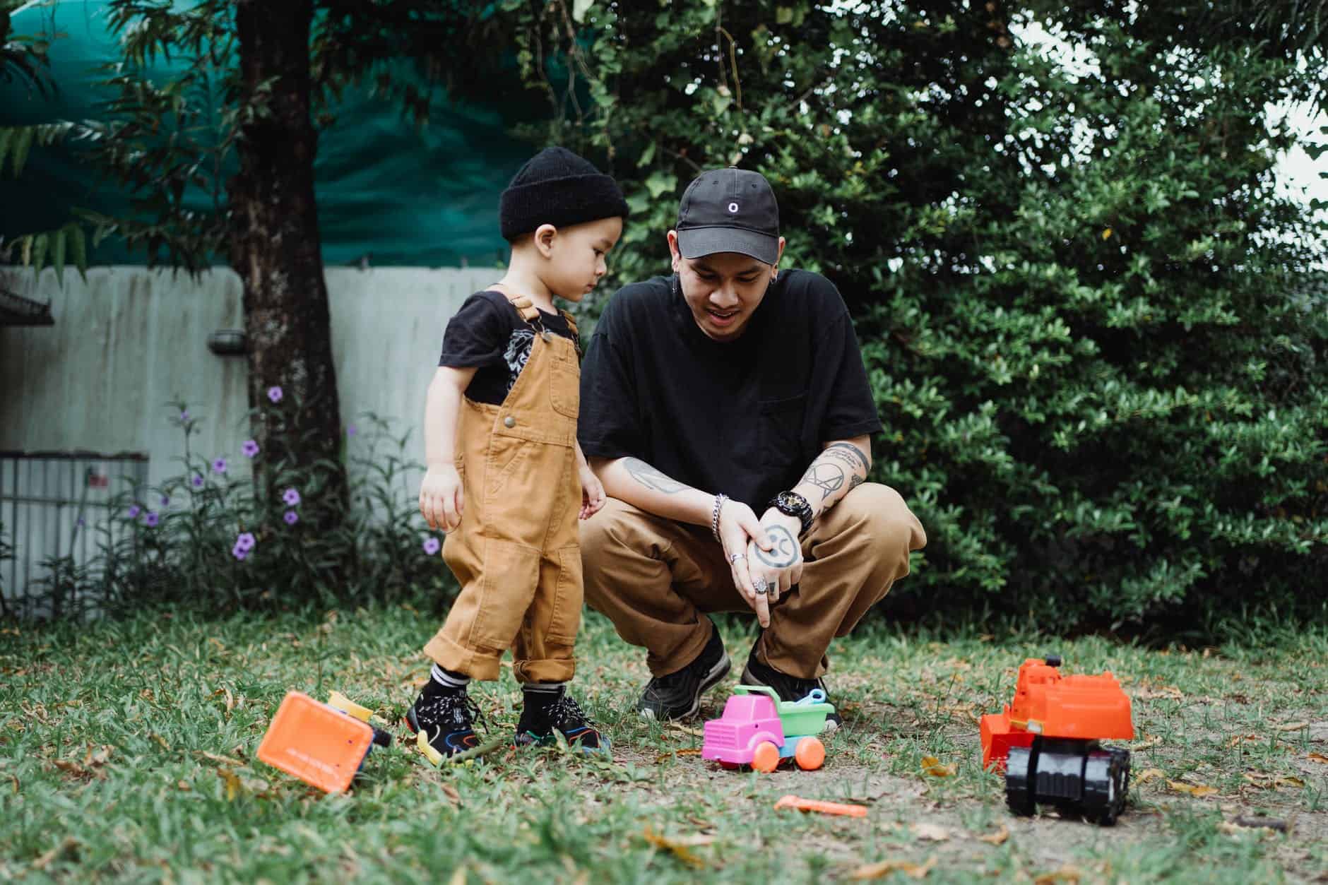 a father and son looking at the toys on the grass