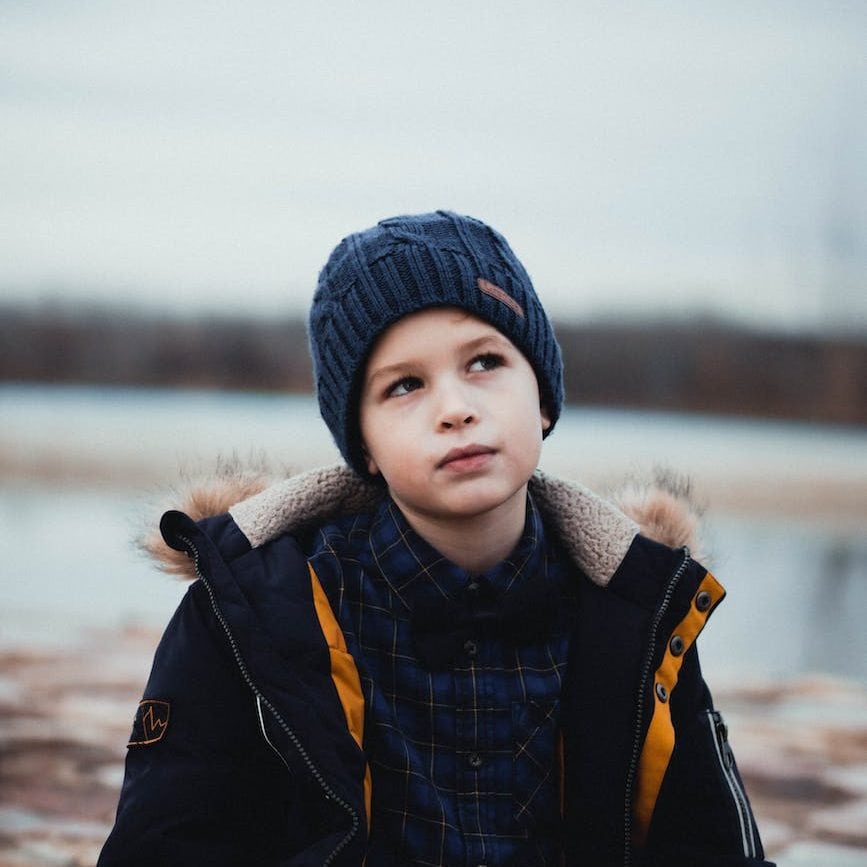 photo of boy thinking while wearing black jacket and blue beanie