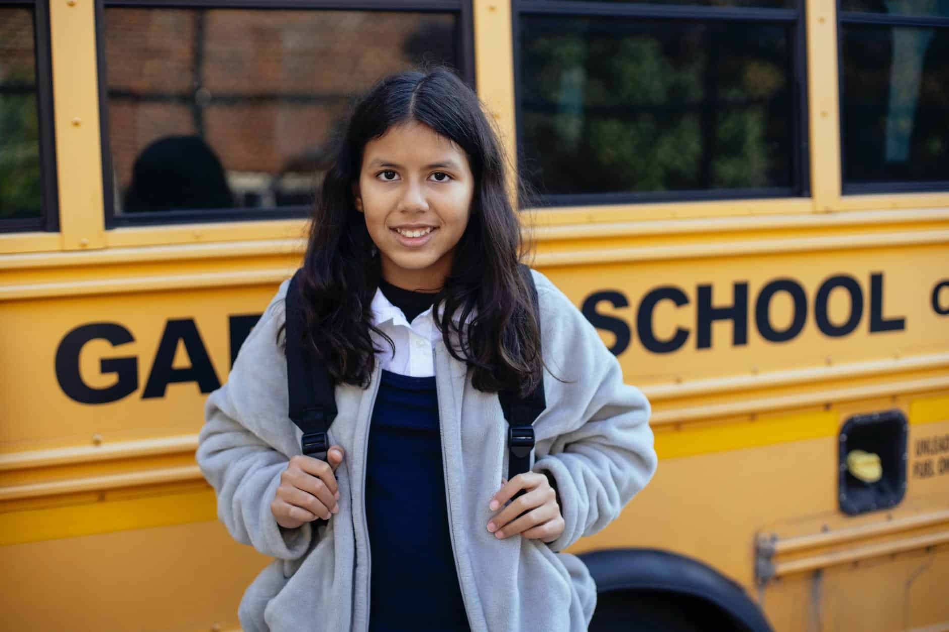 happy hispanic girl near school bus