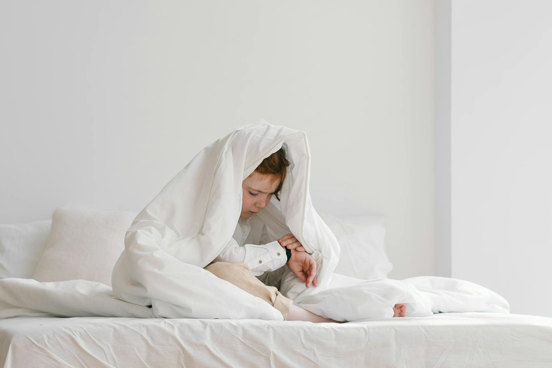little boy sitting on a bed under a duvet